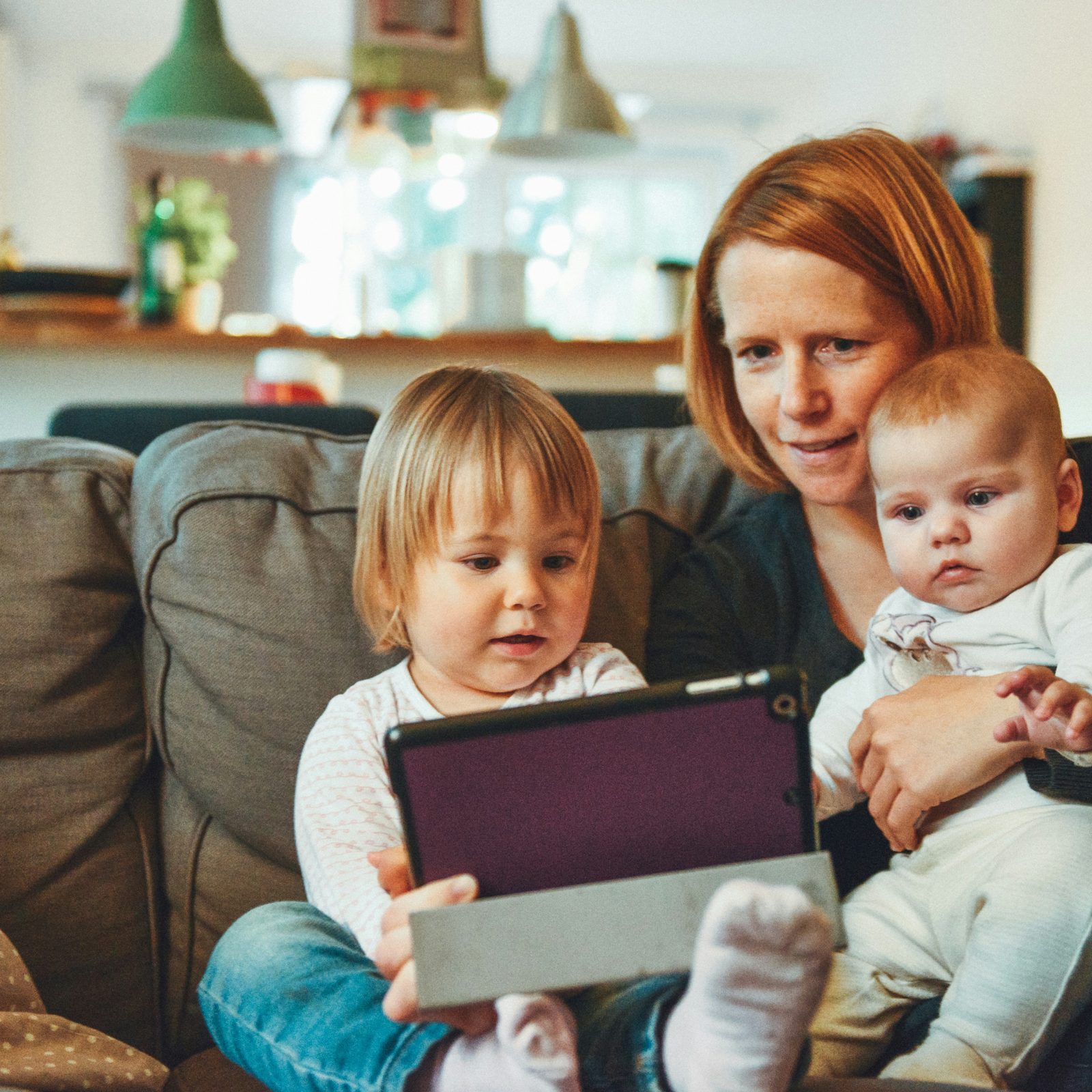 A mother and her two children at home, looking at a tablet together