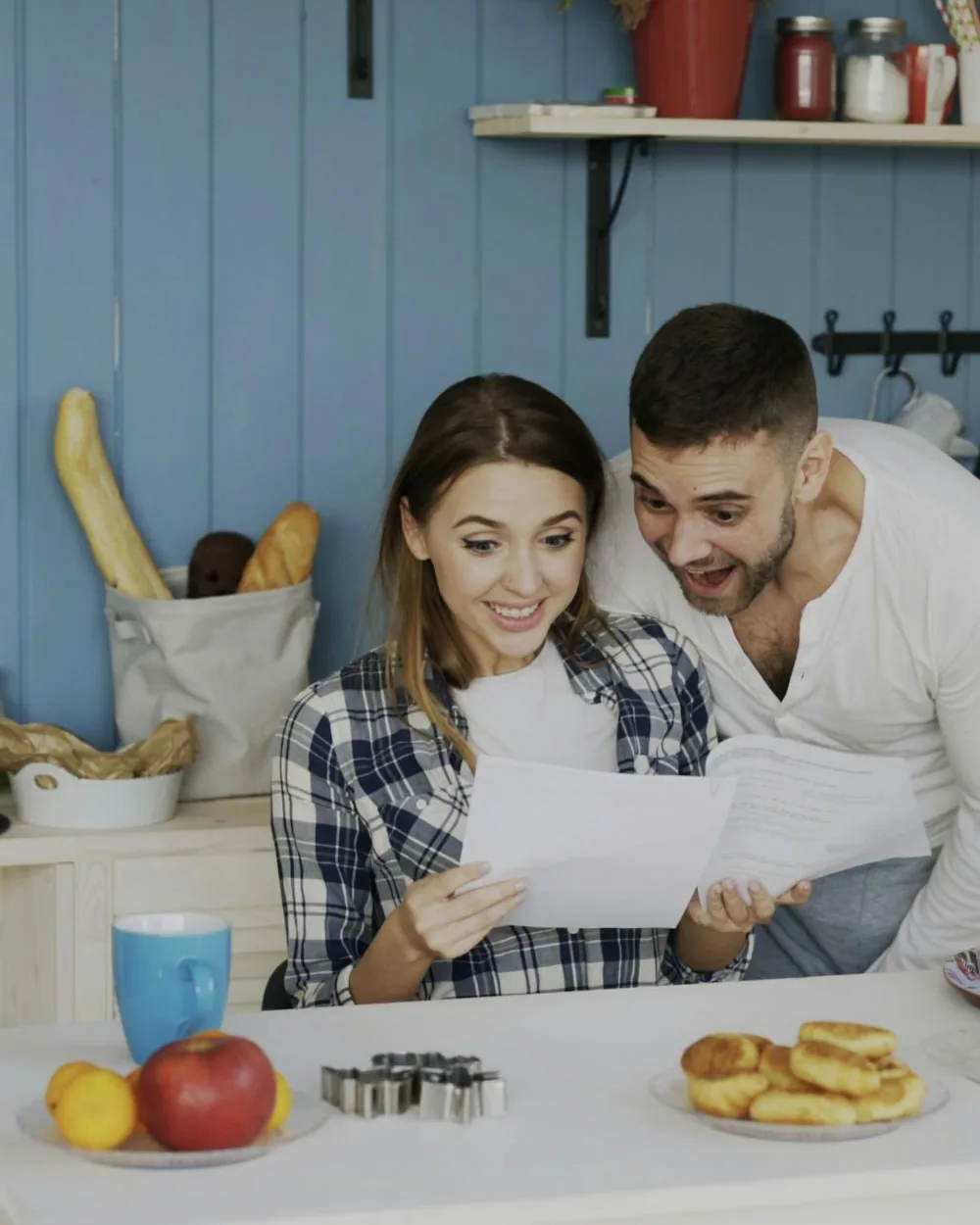 A young couple at their kitchen table, smiling as they read a letter together